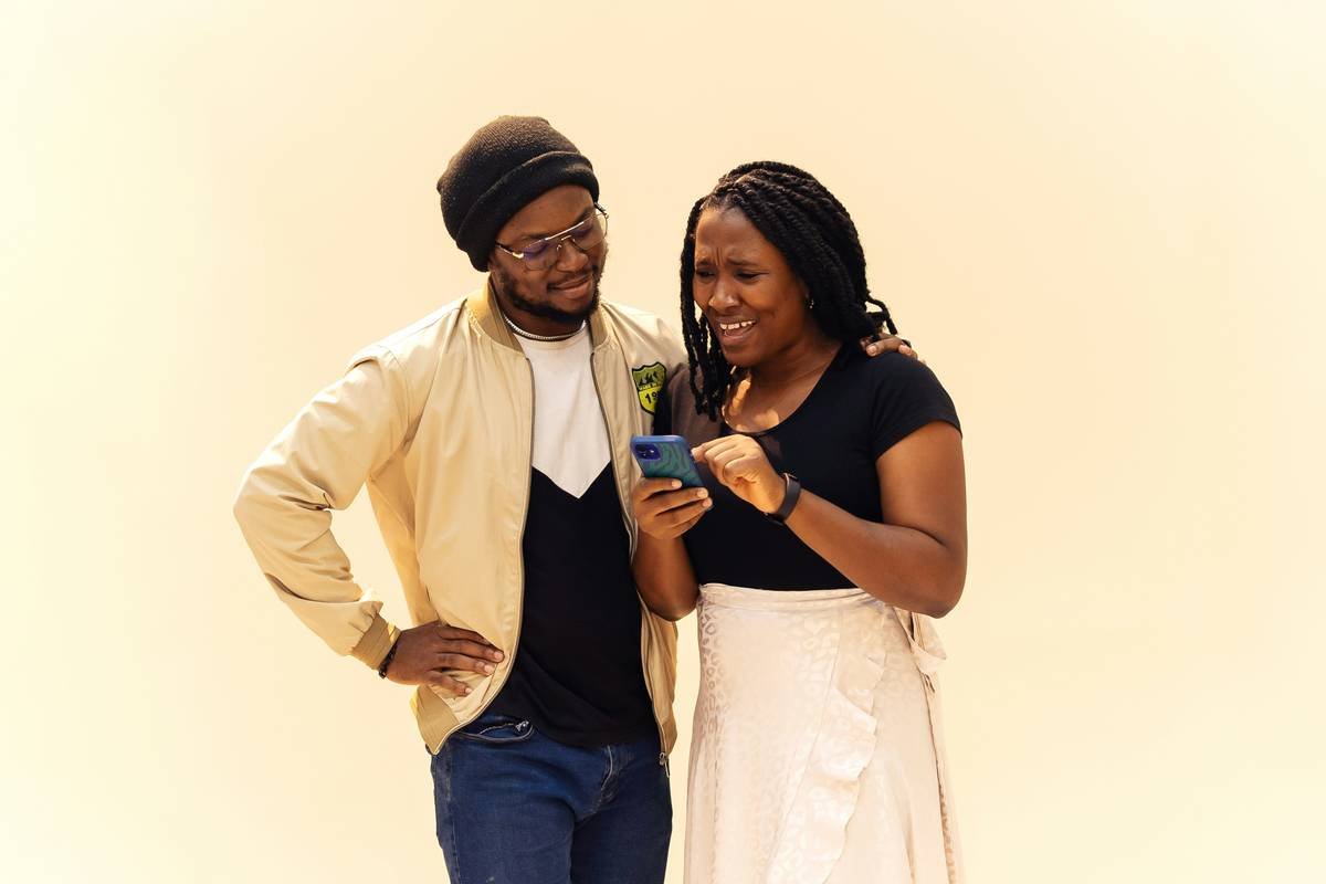 Two friends hanging out. The woman is showing him something to look at on her phone whilst he's smiling at the phone. Find more Afrocentric images at www.ninthgrid.com